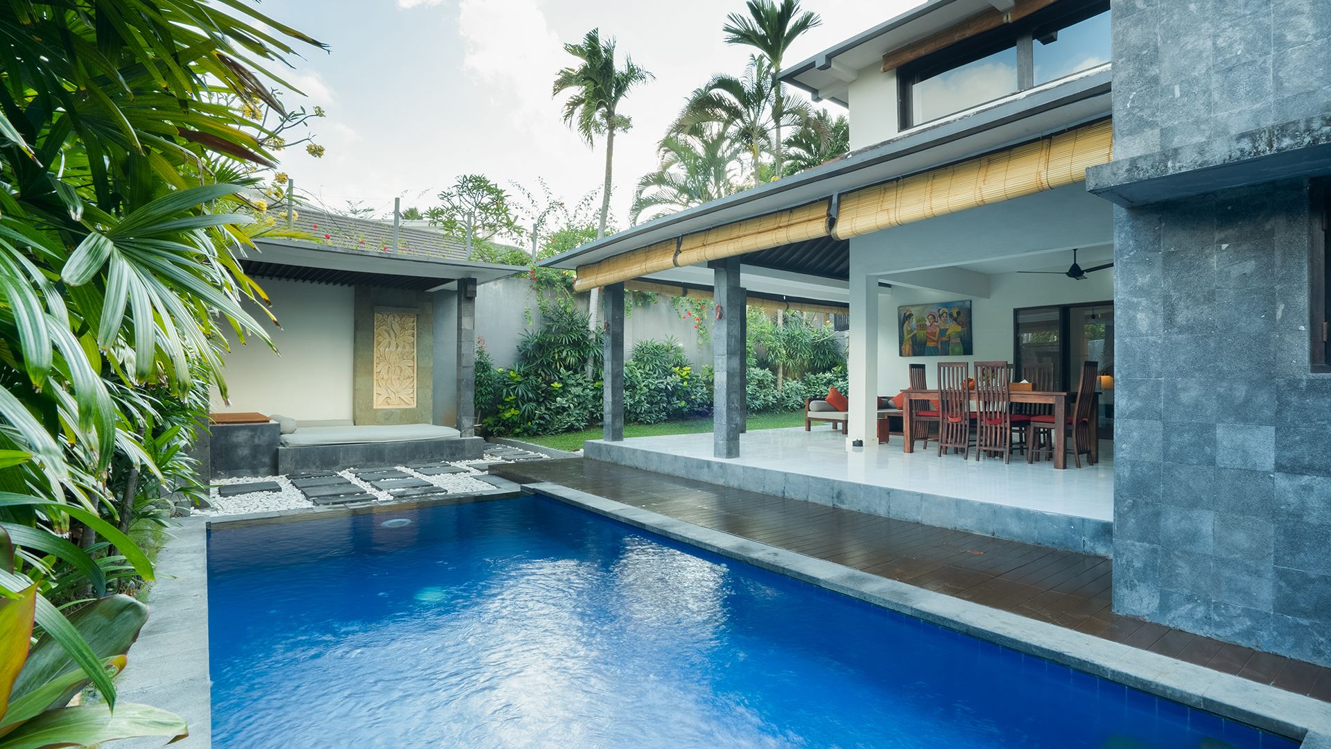 Ein moderner Poolbereich mit einem klaren, blauen Pool, einer überdachten Lounge mit Stühlen und üppiger Bepflanzung.