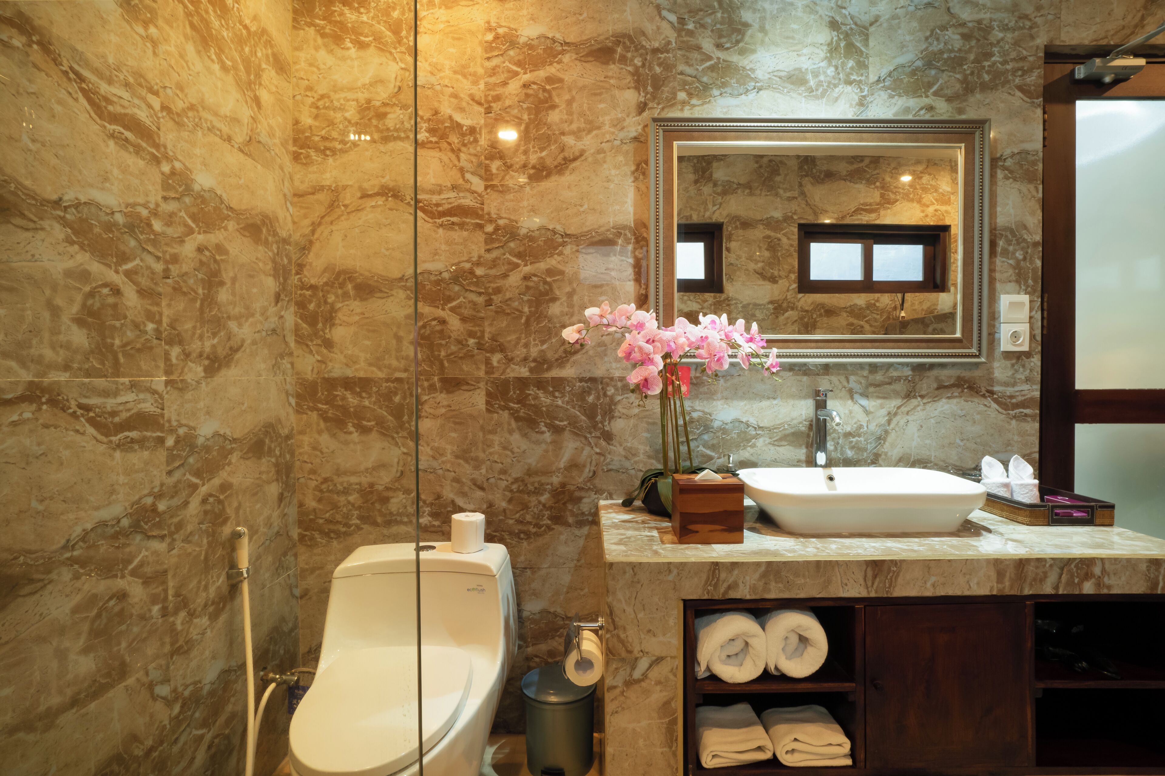 A bathroom with a marble wall, a sink, a mirror, a toilet, and a shower.