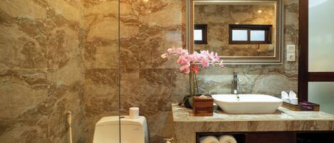 A bathroom with a marble wall, a sink, a mirror, a toilet, and a shower.