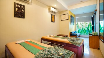 A room with two massage tables, a wooden cabinet, and a window with a green leafy view.