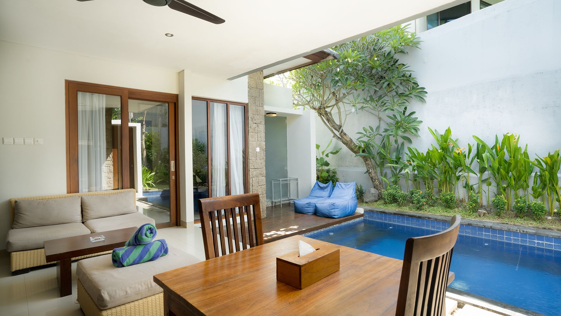 A modern outdoor seating area with a pool, wicker furniture, and a wooden table.