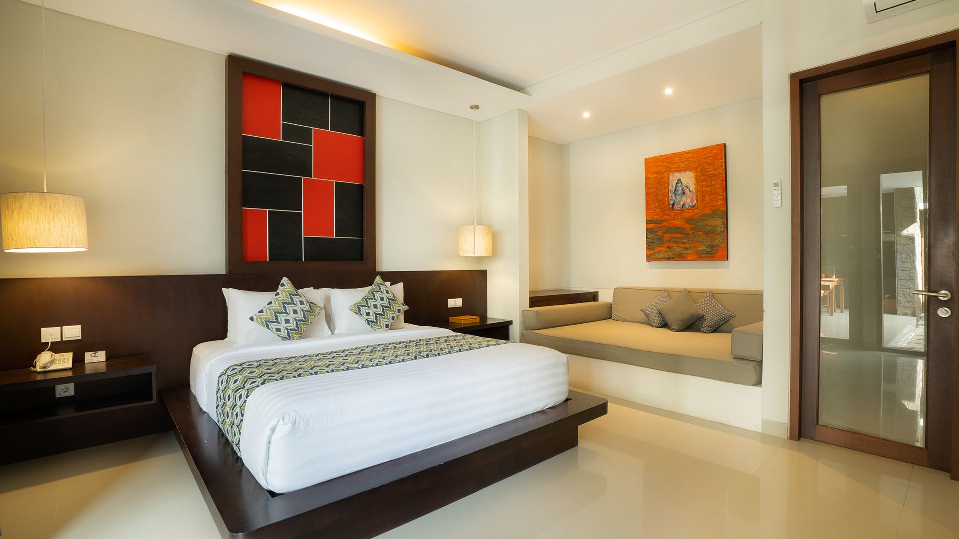 A modern hotel room with a large bed, a sofa, a decorative wall piece, and a glass door.