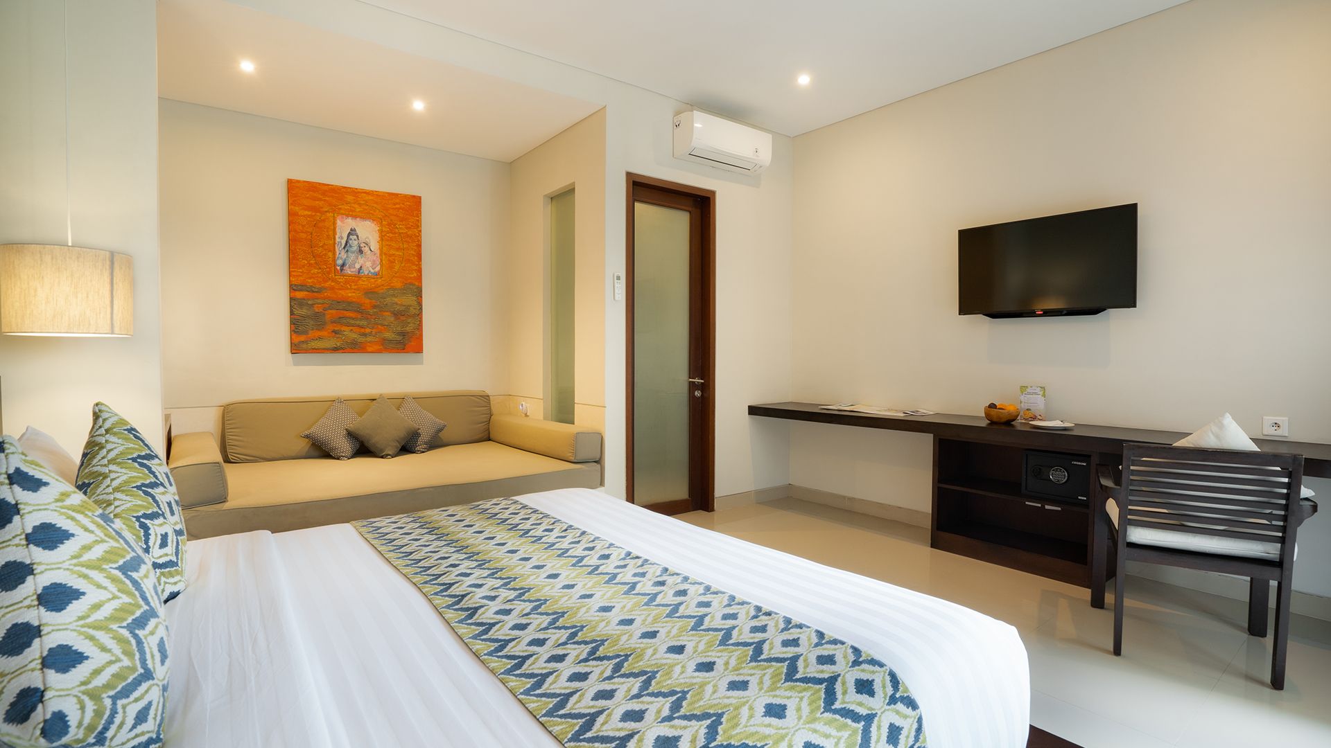 A hotel room with a bed, a sofa, a desk, a television, and an air conditioning unit.