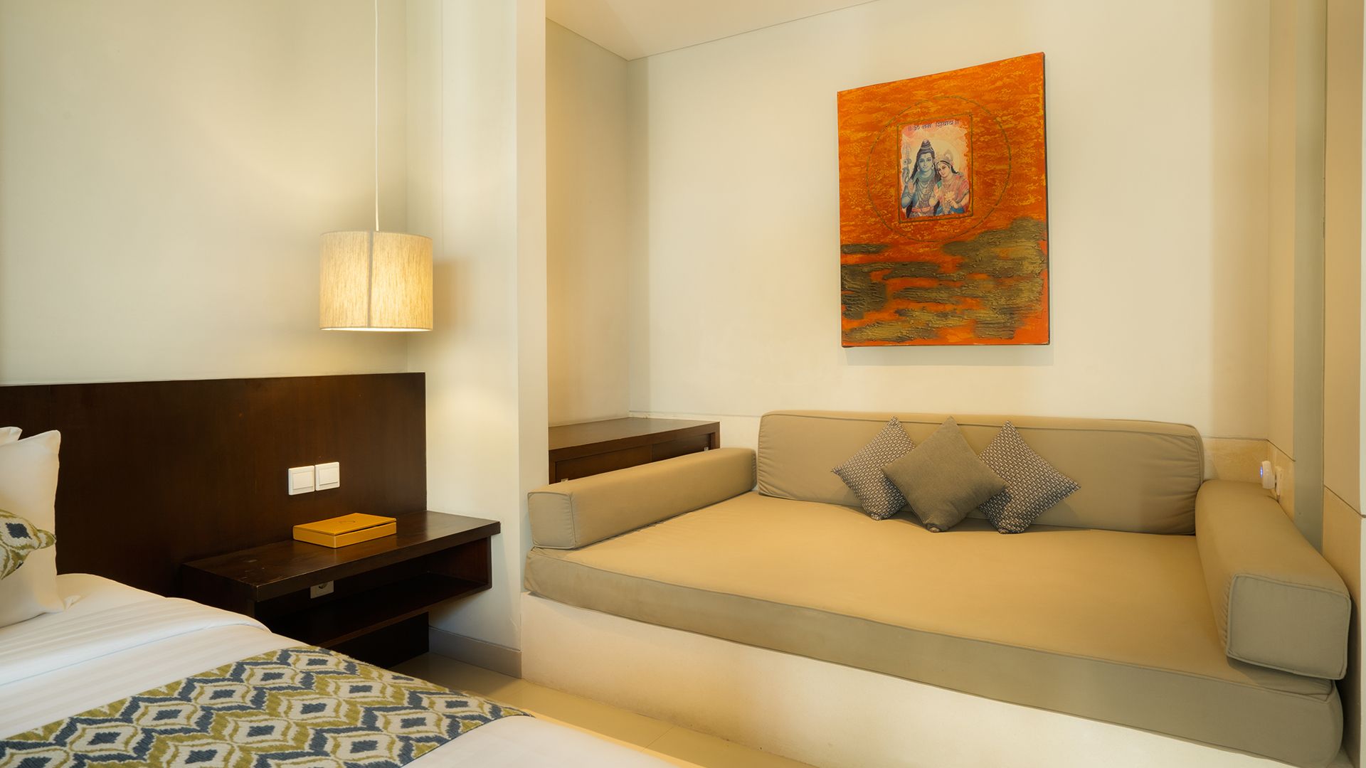 A hotel room with a bed, a sofa, a nightstand, a lamp, and a painting on the wall.