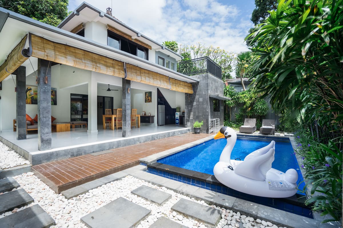 Una casa moderna con piscina, un flotador con forma de cisne y un área de patio techada.