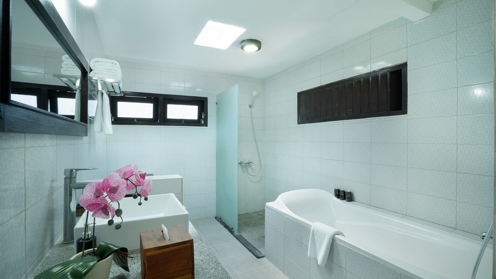 A modern bathroom with a white bathtub, a sink, and a shower. There are towels and a small wooden stool.