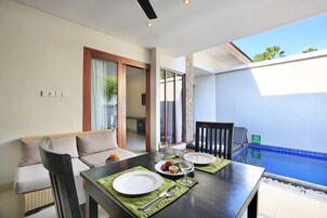 Uma área de refeições com mesa posta para dois, um sofá e vista para uma piscina.