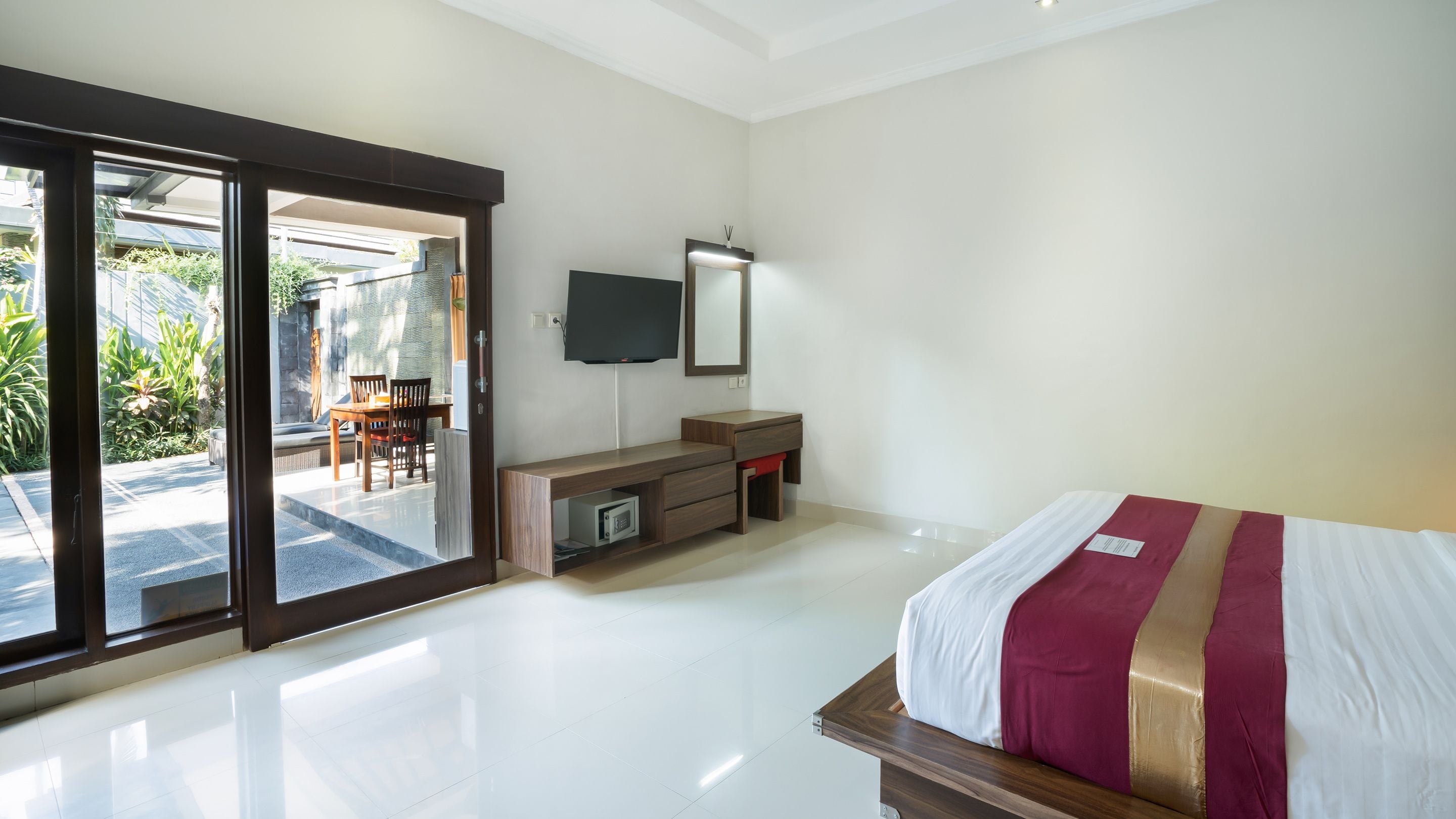 A bedroom with a bed, a desk, a TV, and a sliding glass door leading to an outdoor area.