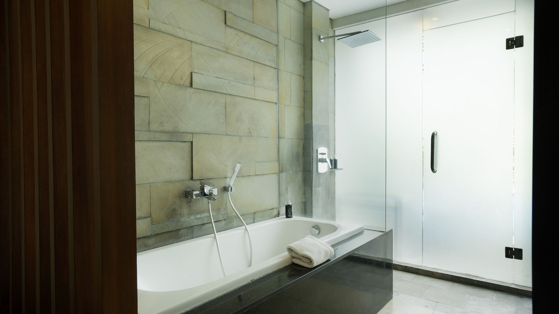 Une salle de bain moderne avec une douche à l’italienne en verre, une baignoire blanche et une serviette posée sur le bord.