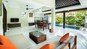 A spacious living area with a flat-screen TV, a dining table with chairs, a coffee table, and a sofa with cushions. - Samaja Beachside Villas (Seminyak)