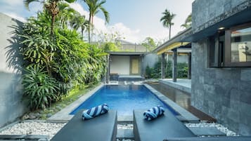 A modern pool area with two lounge chairs and a small pool, surrounded by lush greenery and a stone wall.