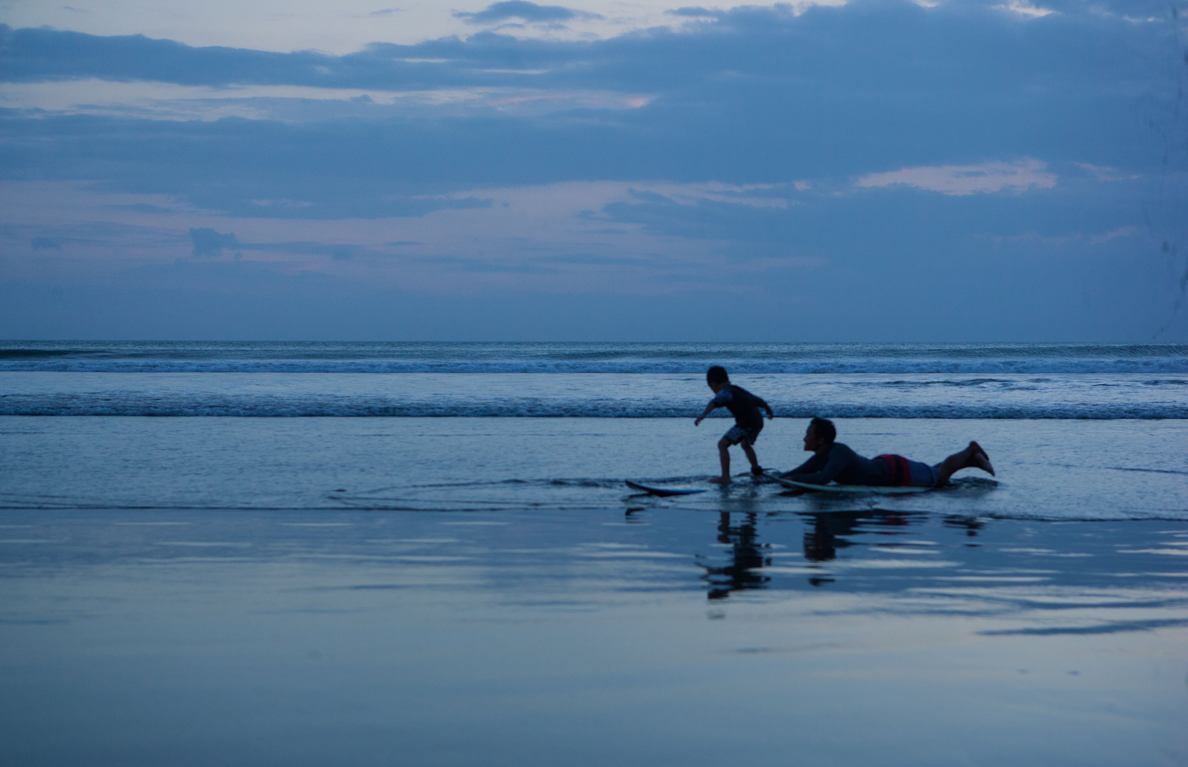 A beach scene with two people, one standing and one lying on the sand, with the ocean in the background.