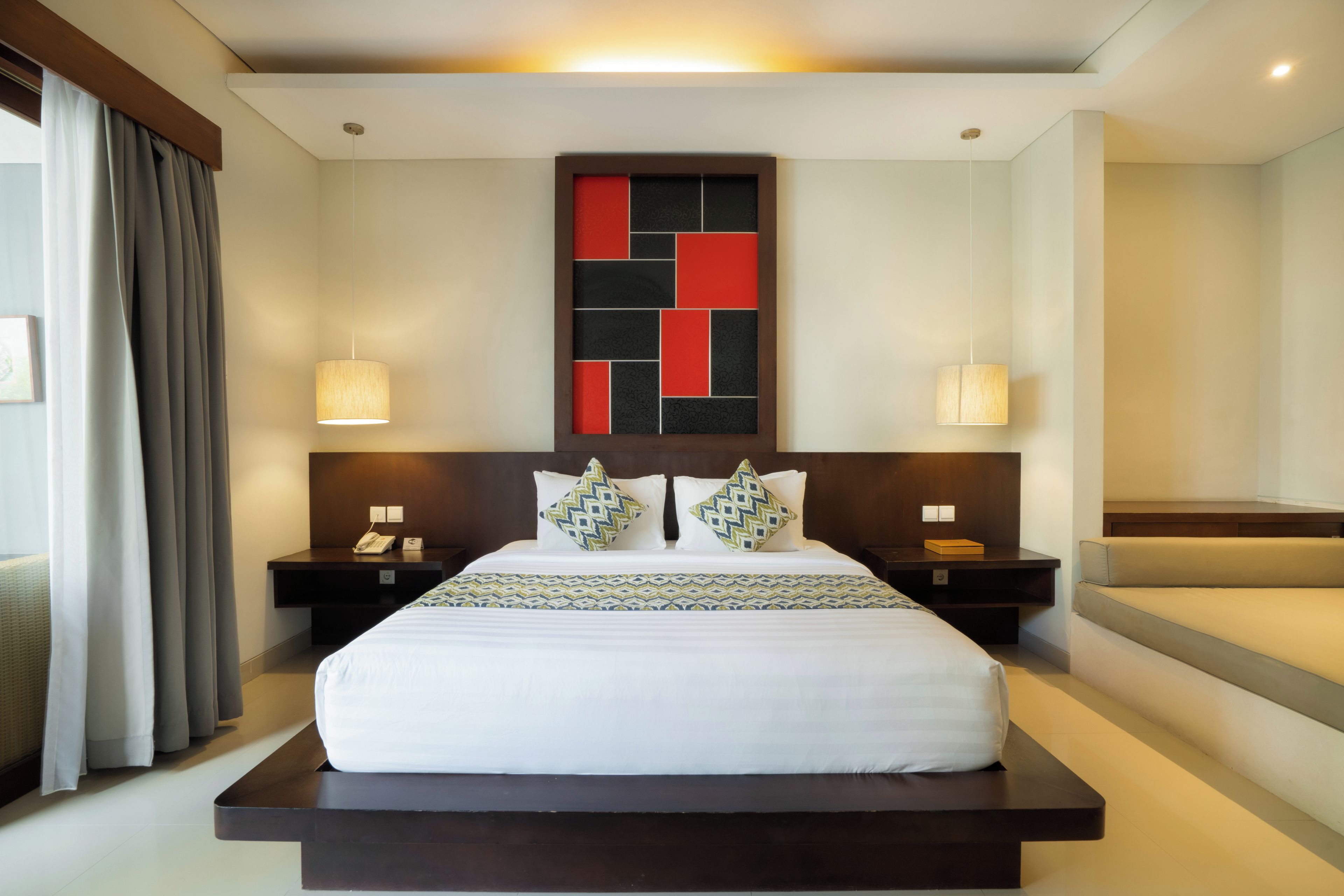 A hotel room with a large bed, two bedside tables, a headboard with a geometric design, and a view of the beach.