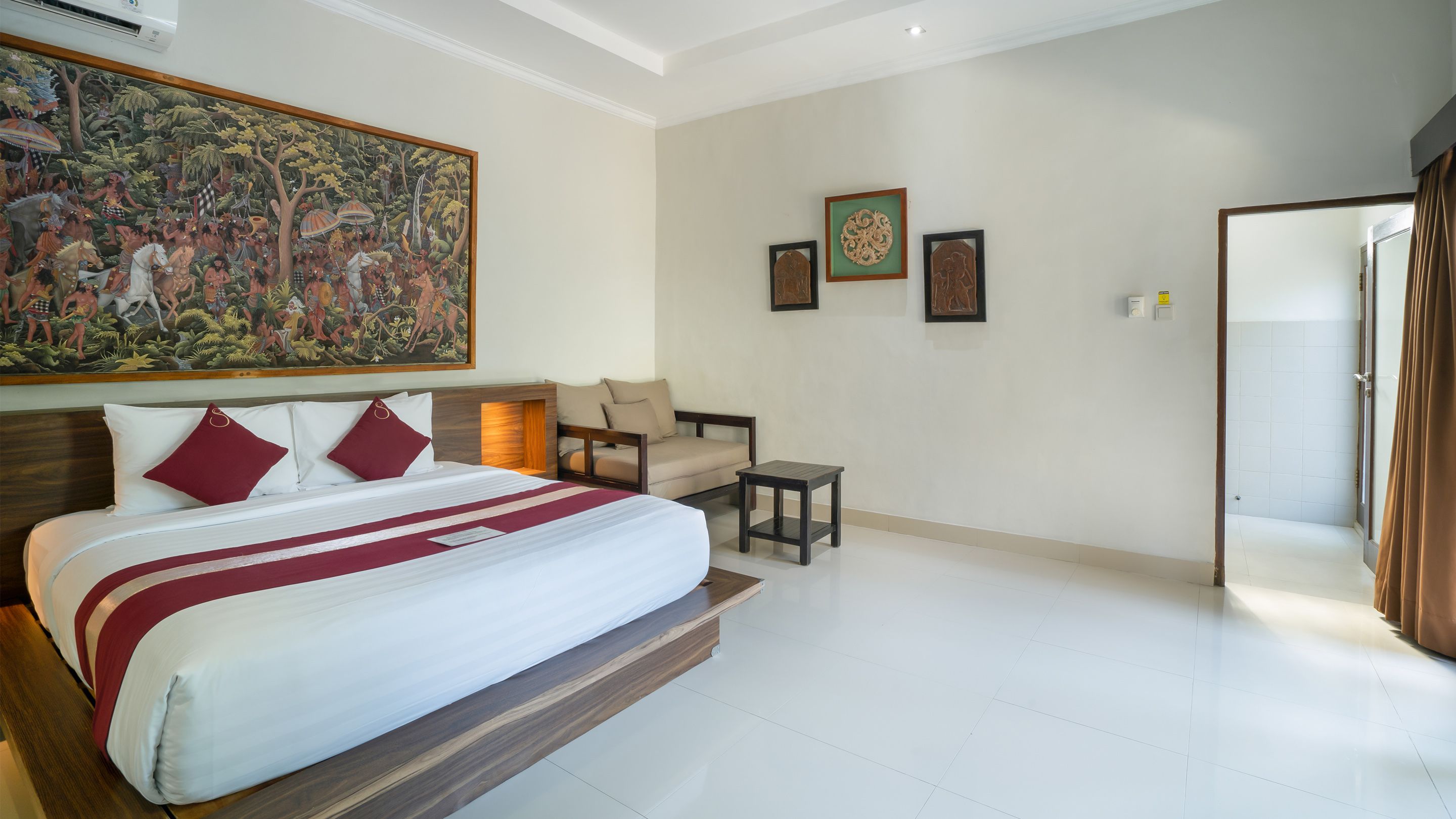 A hotel room with a large bed, a seating area with a sofa and armchairs, a small table, and a painting on the wall.