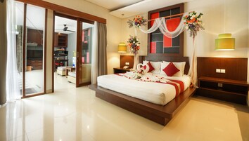 Un dormitorio amplio con una cama grande, un ventanal corredero que da a un balcón y un baño moderno a la vista al otro lado.