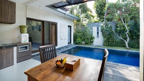 A modern kitchen with a dining area overlooking a swimming pool. - Samaja Beachside Villas (Seminyak)