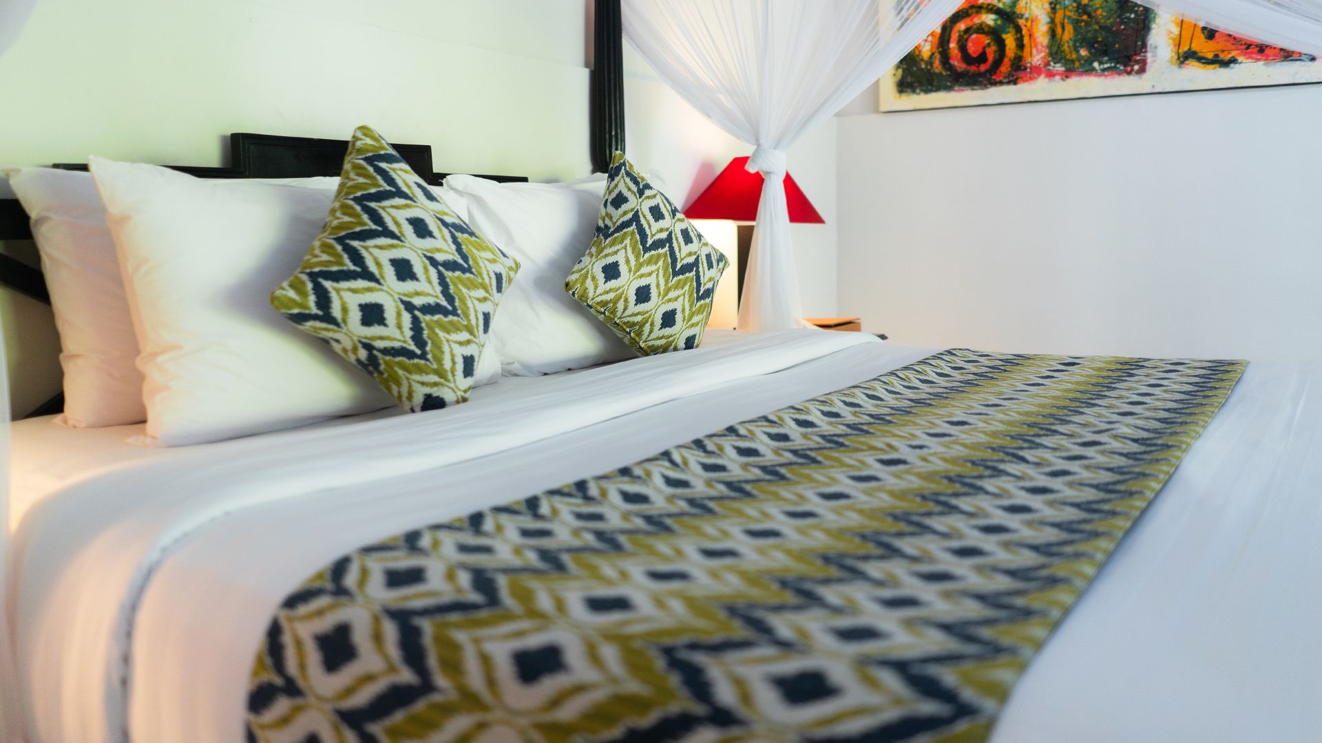 Cama bem arrumada com almofadas estampadas e manta combinando, luminária de cabeceira e pintura na parede.