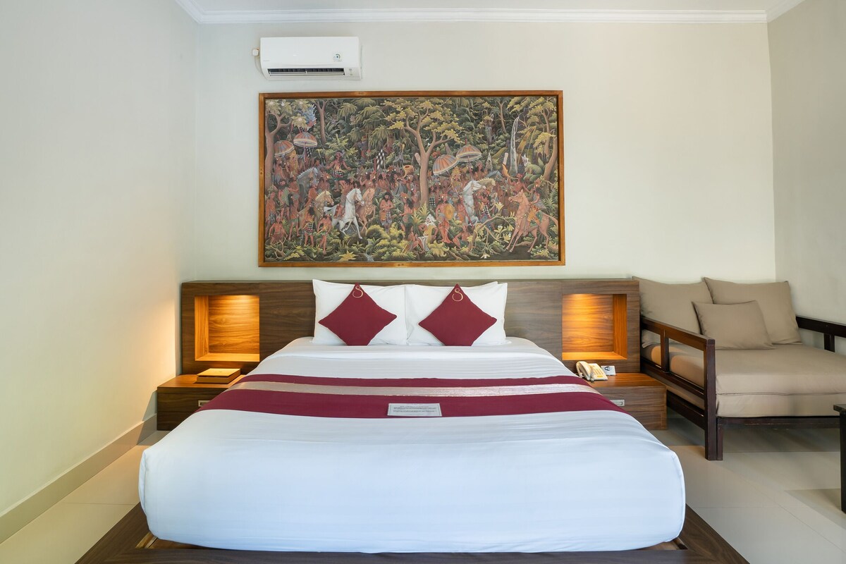 A hotel room with a large bed, a nightstand with a lamp, a chair, and a painting on the wall.