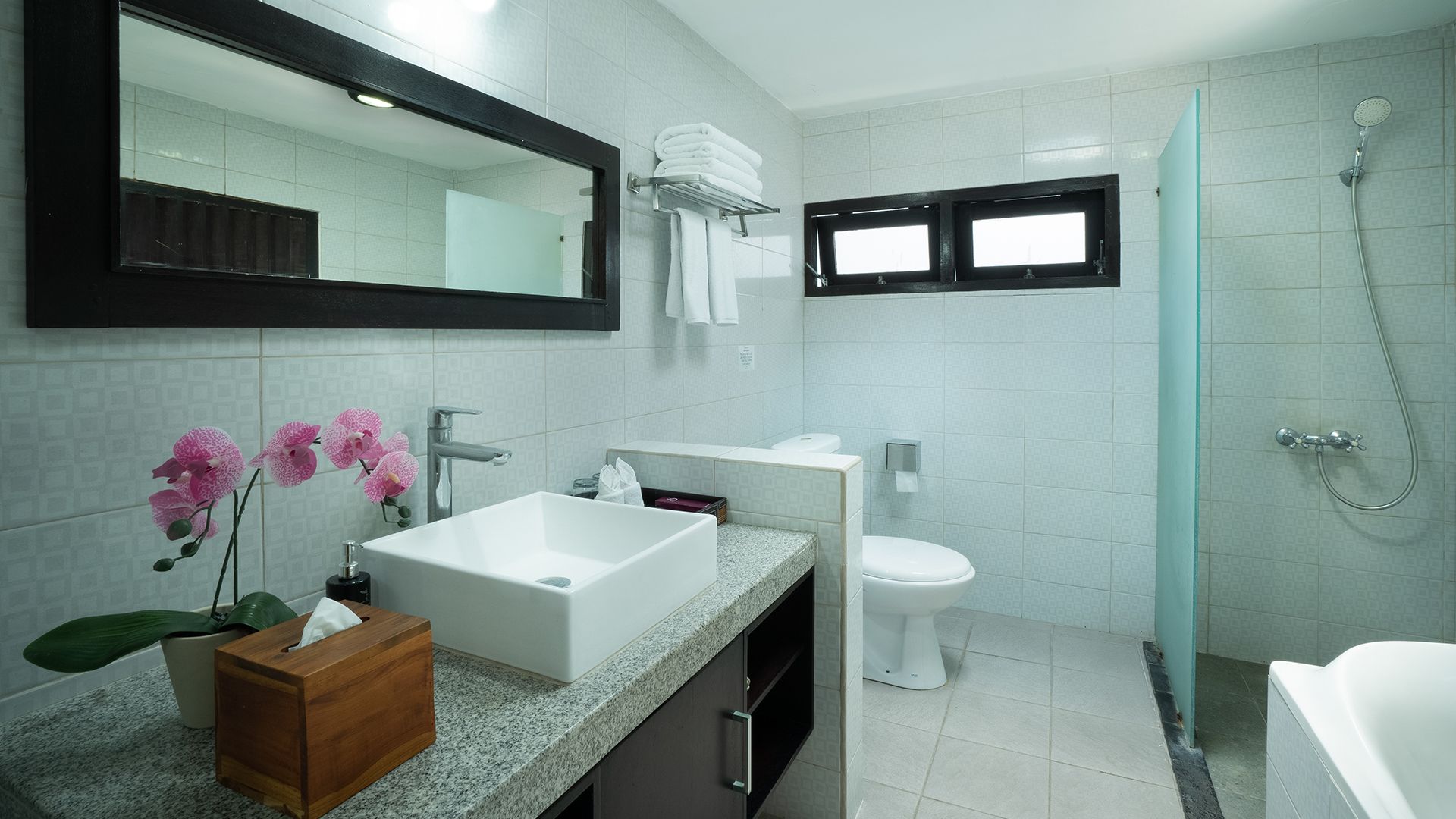 A modern bathroom with a large mirror, white sink, toilet, and a shower area.