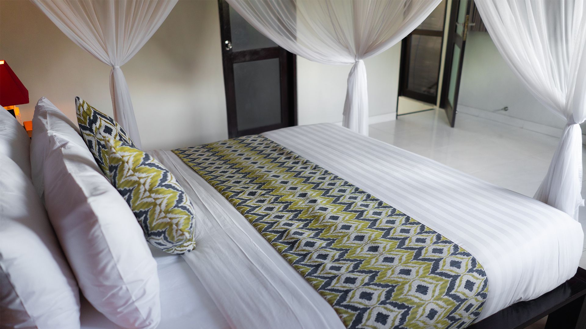 Uma cama com colcha estampada, almofadas brancas e dossel.