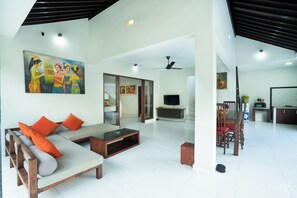 A spacious living area with a sofa, coffee table, and dining table. There is a TV and a painting on the wall. - Samaja Beachside Villas (Seminyak)