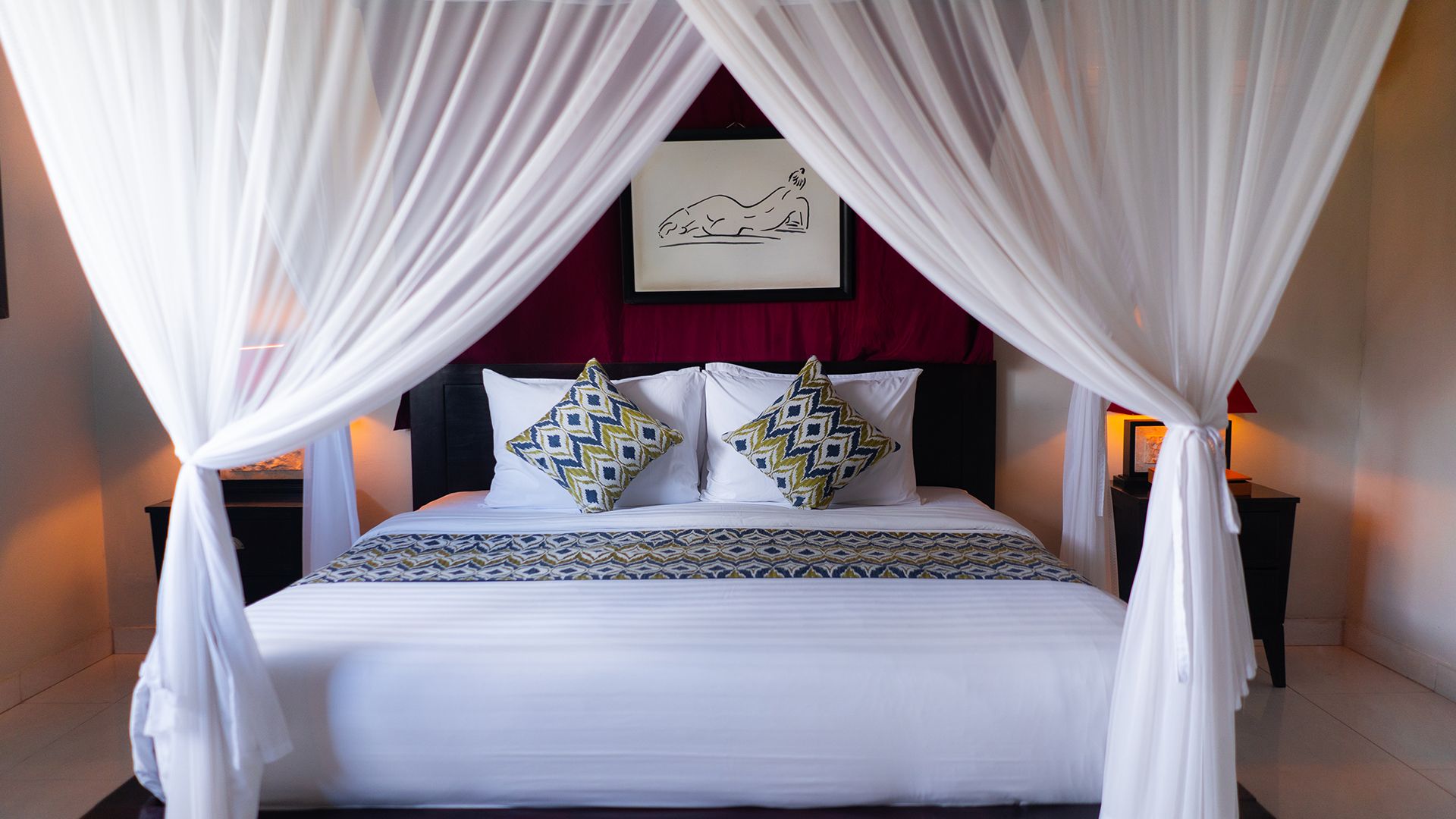 A bed with a canopy, two decorative pillows, a framed artwork above the bed, and bedside lamps.