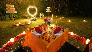 An outdoor dining setup with a heart-shaped light arrangement, tables set with red rose petals, and candle-lit pathways. - Samaja Beachside Villas (Seminyak)