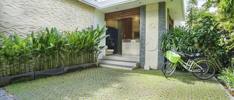 A modern house with a paved courtyard, a bicycle, and lush greenery.