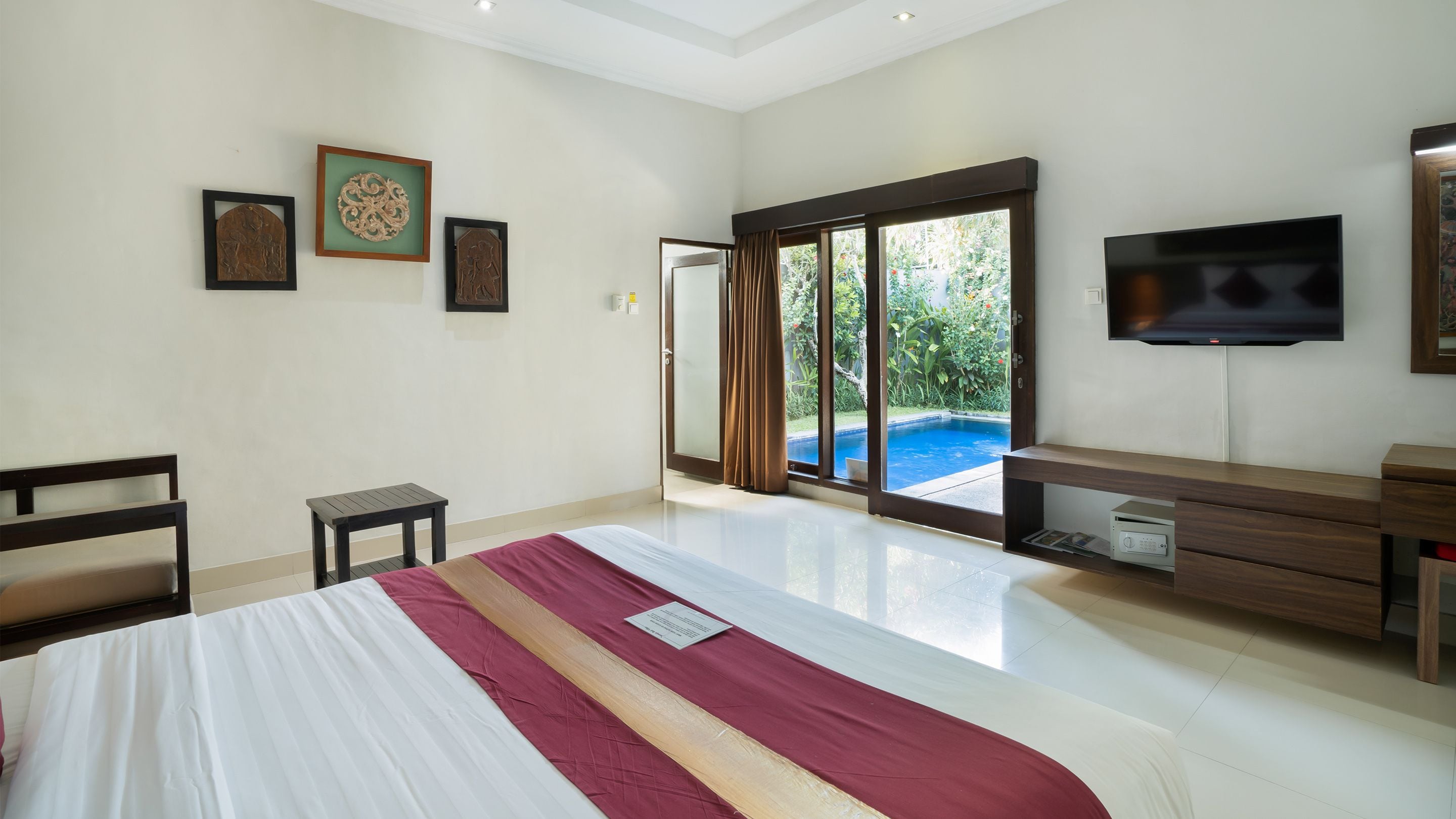 A bedroom with a large bed, a TV, a desk, and a view of a swimming pool.
