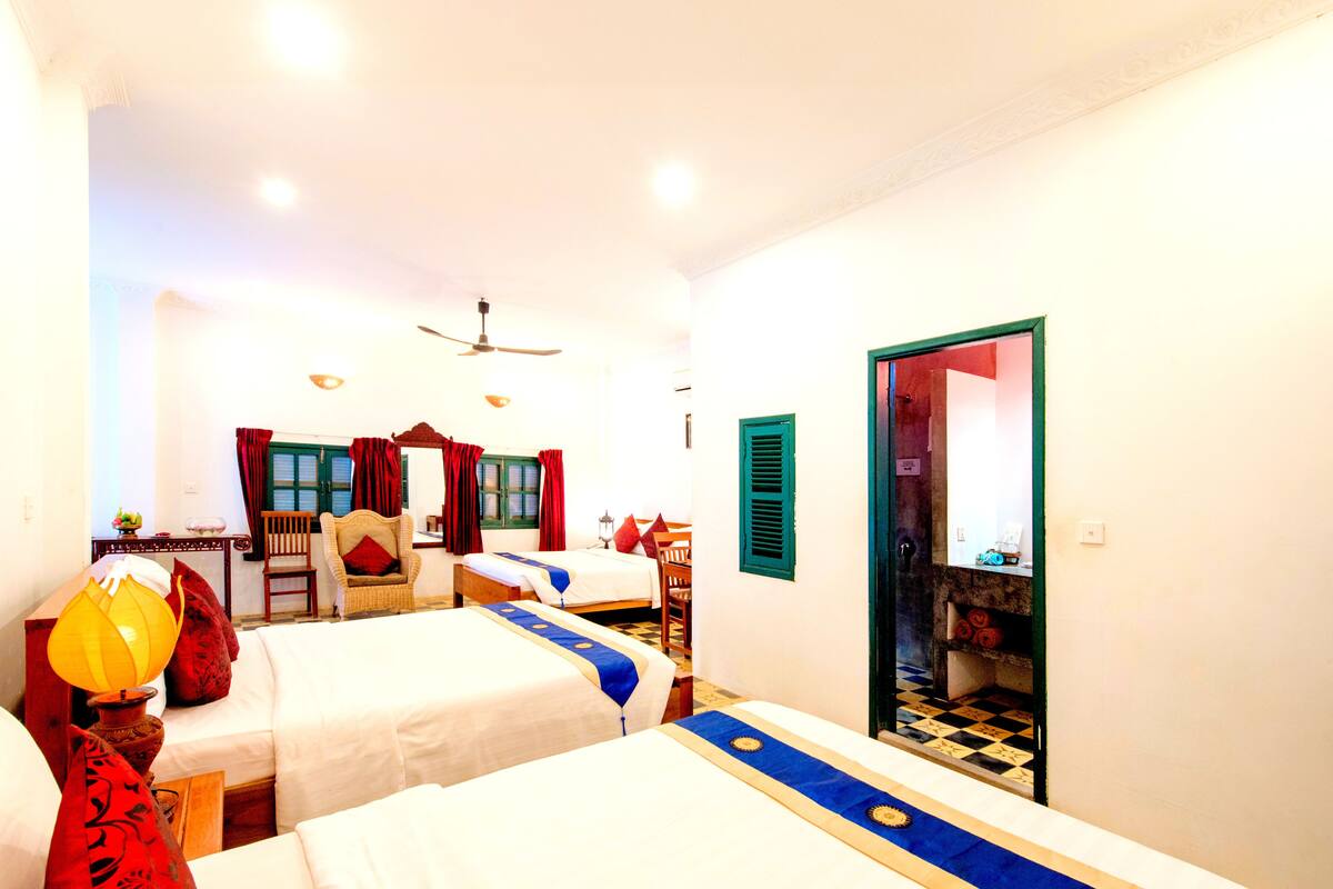 A hotel room with two beds, a sitting area with a chair and table, and a wardrobe.