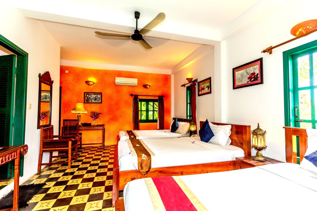 A hotel room with two beds, a ceiling fan, a desk with a lamp, and a window with curtains.
