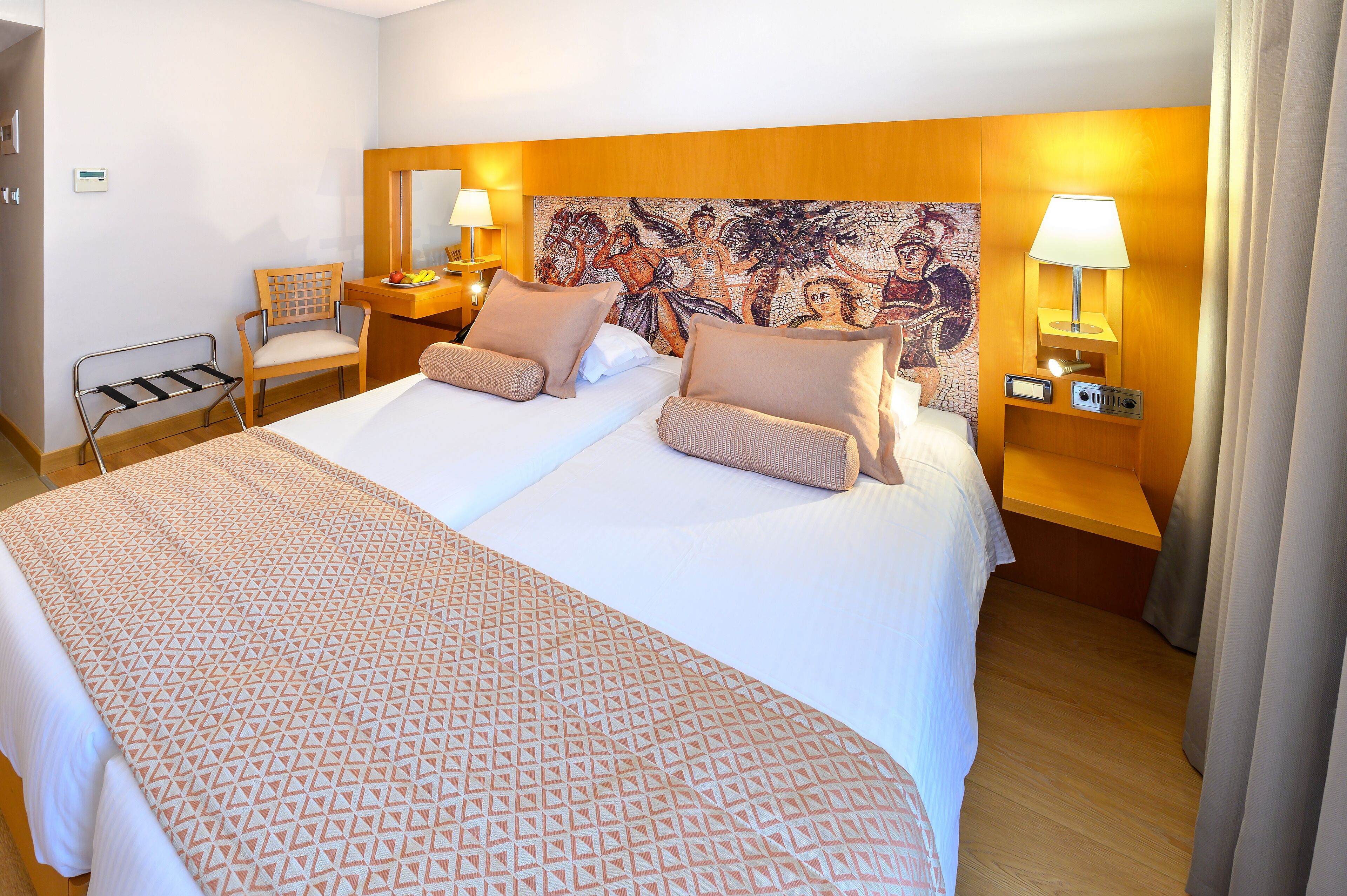 A hotel room with a large bed, two bedside tables, a chair, and a decorative tapestry on the headboard.