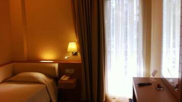 A hotel room with a bed, bedside table with a lamp, a phone, and a window with curtains.