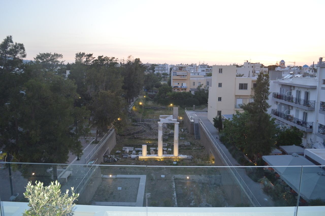 A view of a cityscape with modern buildings, a central open area with columns, and a glass railing in the foreground.