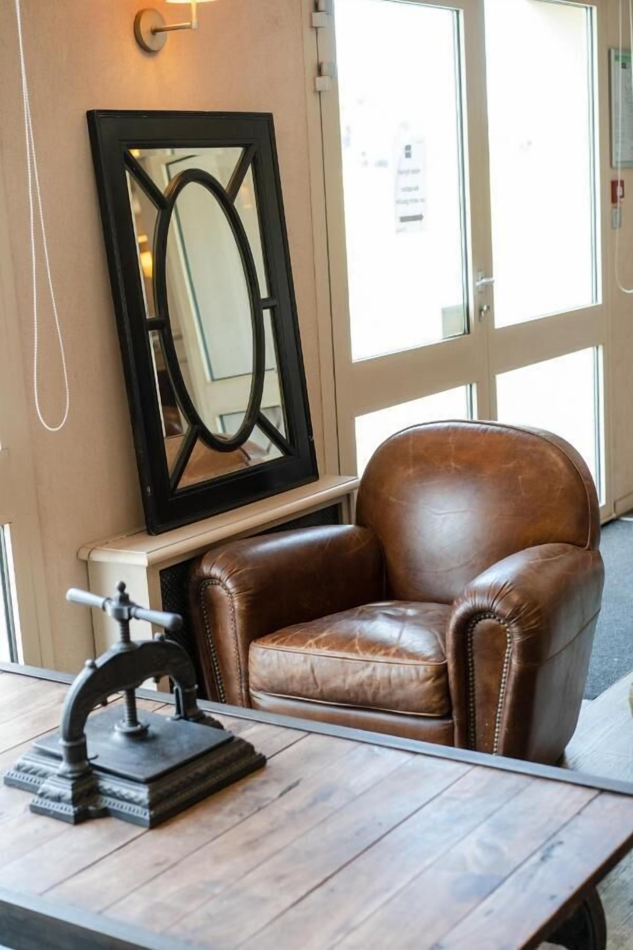 A brown leather armchair in a room with a large mirror and a small table with a decorative object.