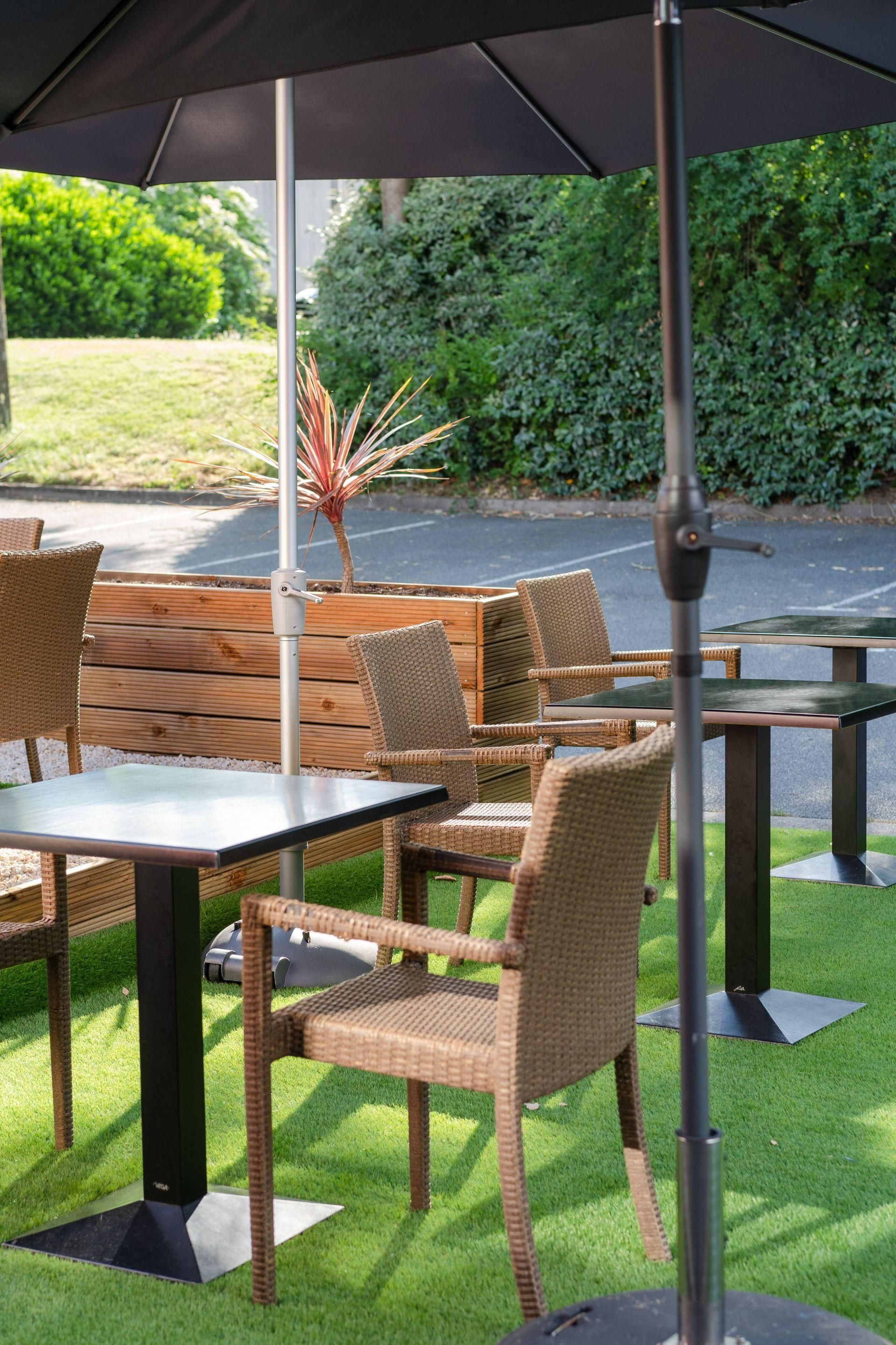An outdoor seating area with wicker chairs and tables, a central plant, and a metal pole.