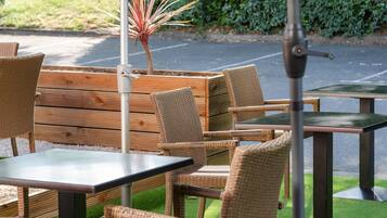An outdoor seating area with wicker chairs and tables, a central plant, and a metal pole.