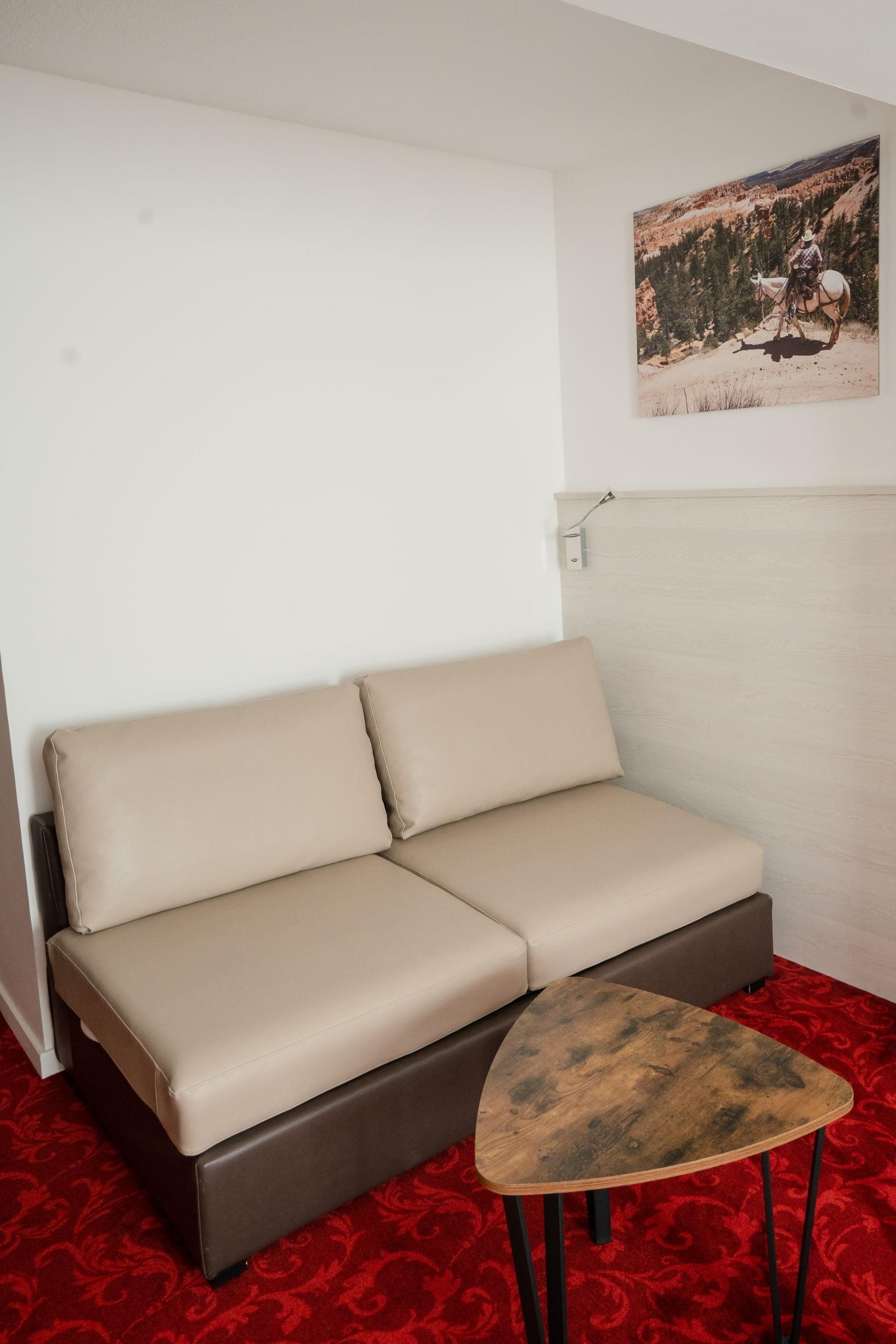 A room with a beige sofa, a small wooden table, and a red patterned carpet.