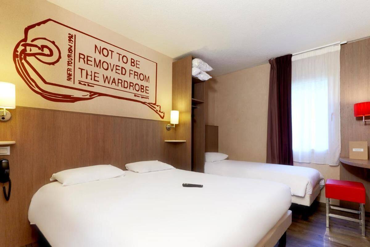 A hotel room with two beds, a red bench, a wall-mounted phone, and a sign with a message.