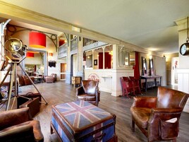 Un hall d’entrée spacieux, doté de fauteuils en cuir, d’un pouf orné du motif Union Jack et d’un coin bar agrémenté d’un rideau rouge.