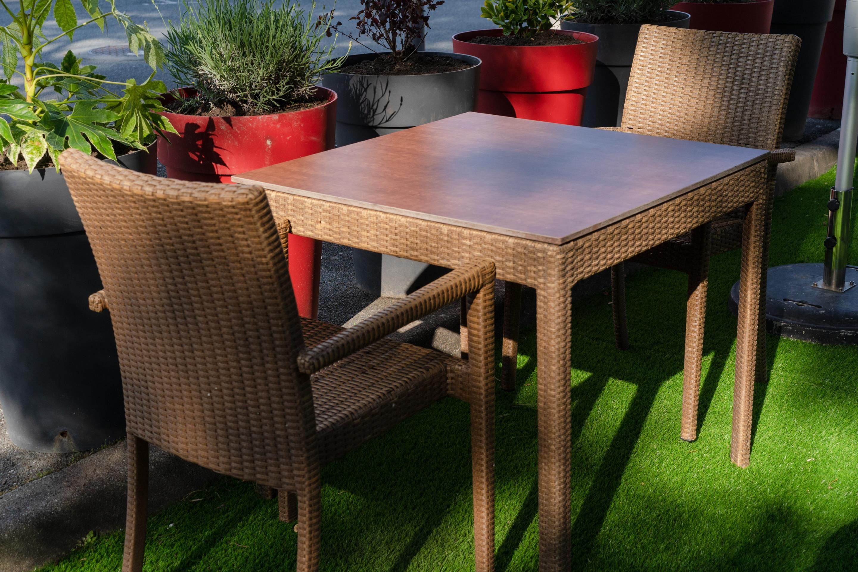 Conjunto de mesa e cadeiras de vime sobre grama artificial, com vasos de plantas ao redor.