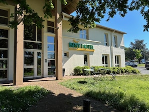 A hotel building with a sign reading 'BRIT HOTEL' and a paved entrance area with outdoor seating. -  Brit Hotel Essentiel CHOLET (Cholet)