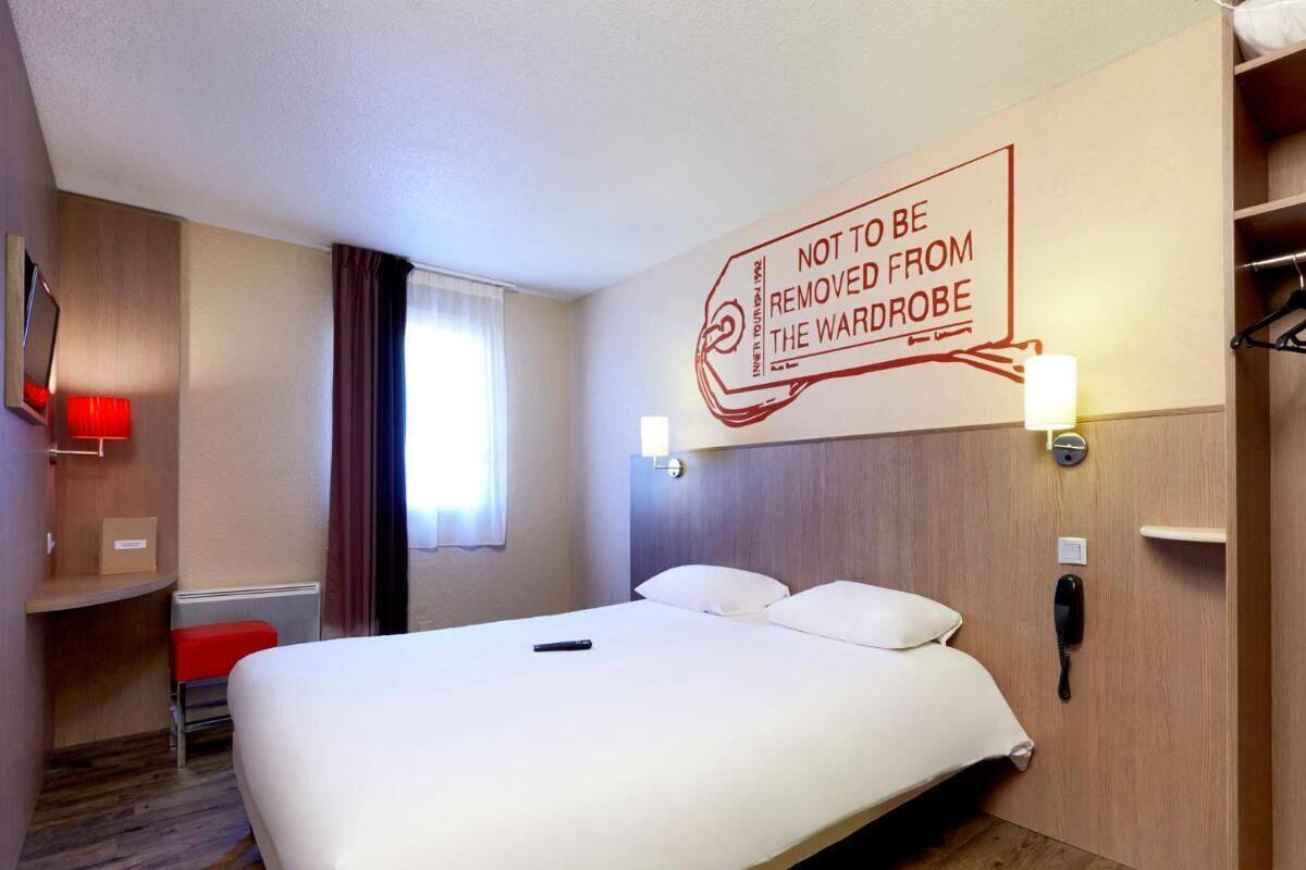 A hotel room with a large bed, a bedside table, a red chair, a wardrobe, and a wall-mounted sign.