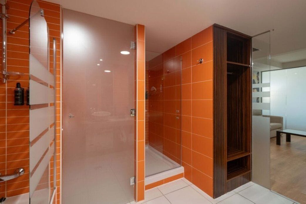Un bany modern amb rajoles taronja, una cabina de dutxa de vidre i un tocador de fusta.
