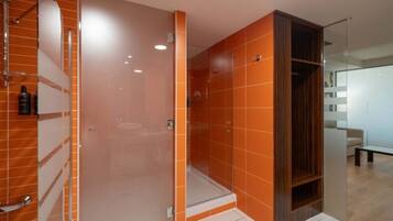 Un bany modern amb rajoles taronja, una cabina de dutxa de vidre i un tocador de fusta.