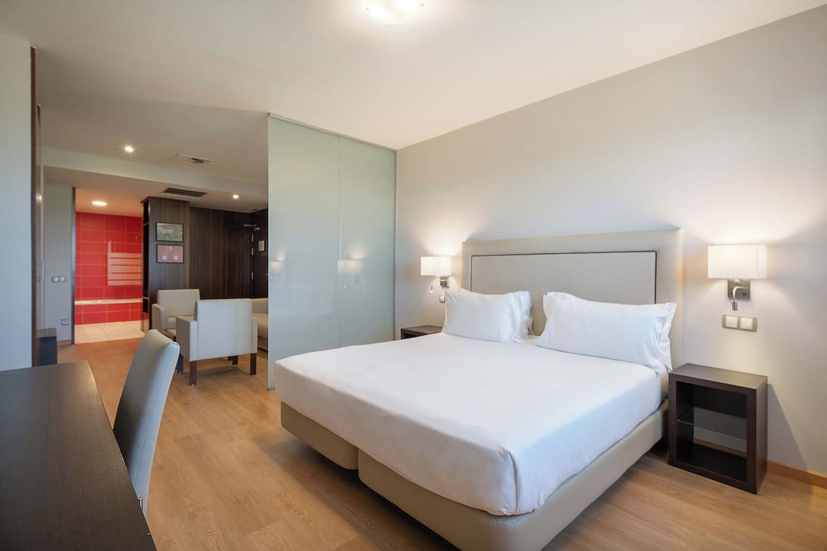 A hotel room with a bed, two bedside tables, a desk, and a chair.