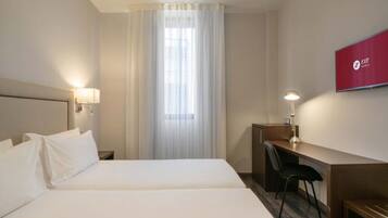 Een hotelkamer met een bed, een bureau, een stoel, een televisie en een raam met gordijnen.