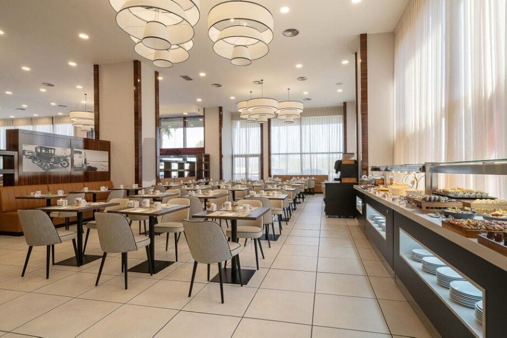 Un vaste espace dédié à la salle à manger, avec de nombreuses tables et chaises, un buffet proposant une variété de plats, et de grandes fenêtres laissant entrer la lumière naturelle.