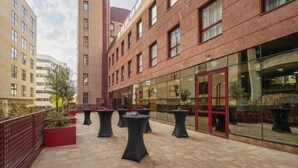 A courtyard with outdoor seating and a glass building facade. - Exe Convention Plaza Madrid (Madrid)