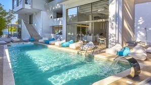 Un área de piscina exterior moderna con una piscina azul cristalina, sillones de descanso blancos y una escalera que lleva a un nivel superior.